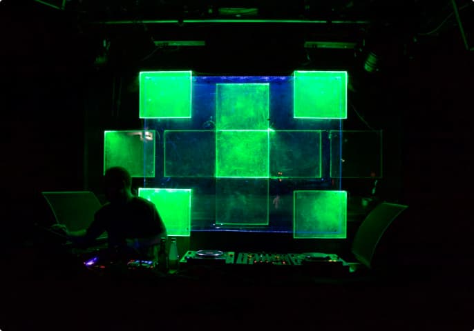 A DJ booth with square-shaped acrylic glass behind it that are glowing in green colors