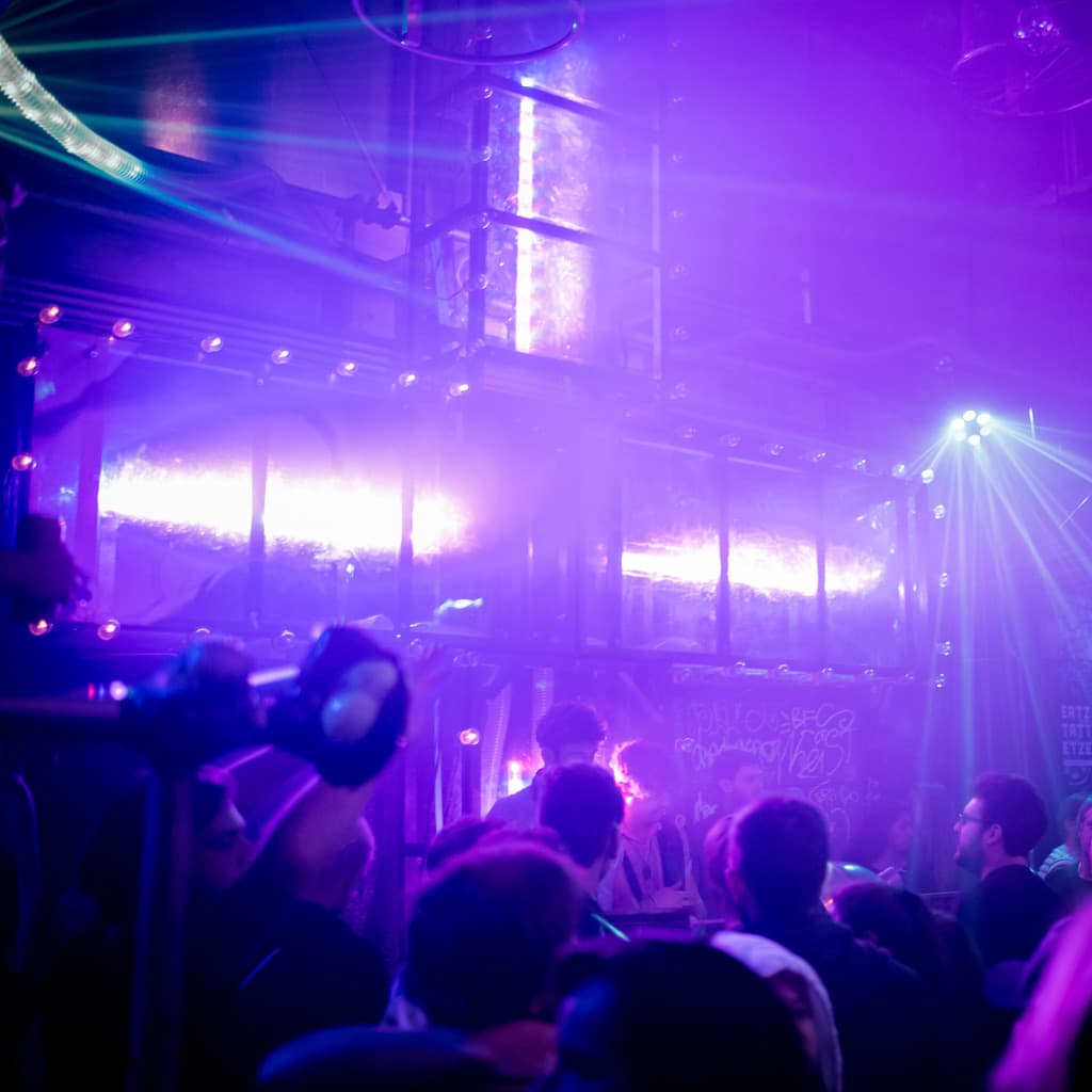 © Christopher Glanzl - Kultur For President 2018 - Flucc - Plus Installation A filled club with DJs and a giant plus with bright purple lights behind them