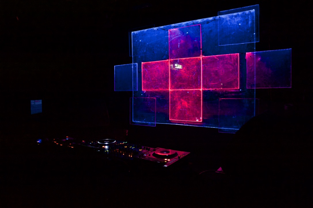 © James Morrison-Knight - Kultur For President 2019 - Acrylic glass installation 3 A DJ booth with square-shaped acrylic glass behind it that are glowing in red and blue colors
