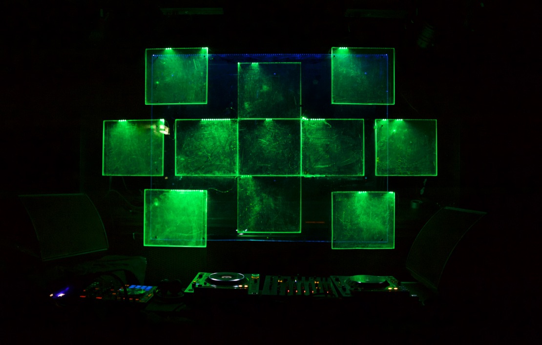 © James Morrison-Knight - Kultur For President 2019 - Acrylic glass installation 2 A DJ booth with square-shaped acrylic glass behind it that are glowing in green colors