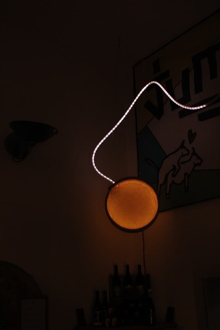 Jumi Käse Installation 2018 - Inside the store A circled shaped object that diffuses mild yellow LED lights coming from inside of the object. The object hangs on the ceiling in a cheese store and another LED hose hanging on top of it